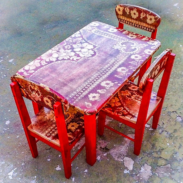 A kid’s table & chair set with a distressed, red, lace pattern, over stained, solid wood. 