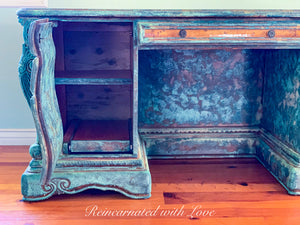 Close up of an open, cabinet door on a boho style desk, shows additional storage space & details in the desk’s patina finish.