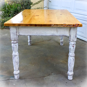 The side view of a farmhouse style, dining table, painted in distressed white, with a reclaimed wood tabletop.