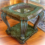 A boho style, vintage, end table, made of solid wood, with a rusted copper, green patina finish & a beveled, glass tabletop.