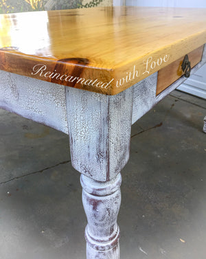 Close up of the wood grain on a knotted pine tabletop, done in stained wood with a white, shabby chic style base.