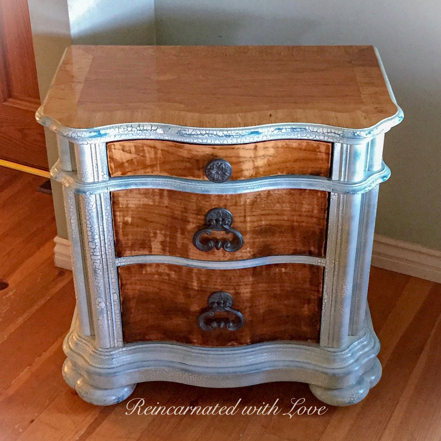Farmhouse nightstand with three large drawers, done in a shabby chic, white finish with stained wood tabletop & drawer faces.