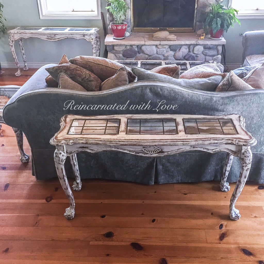 A living room with two, French country style, sofa tables, painted in distressed white with glass panels in the tabletops.