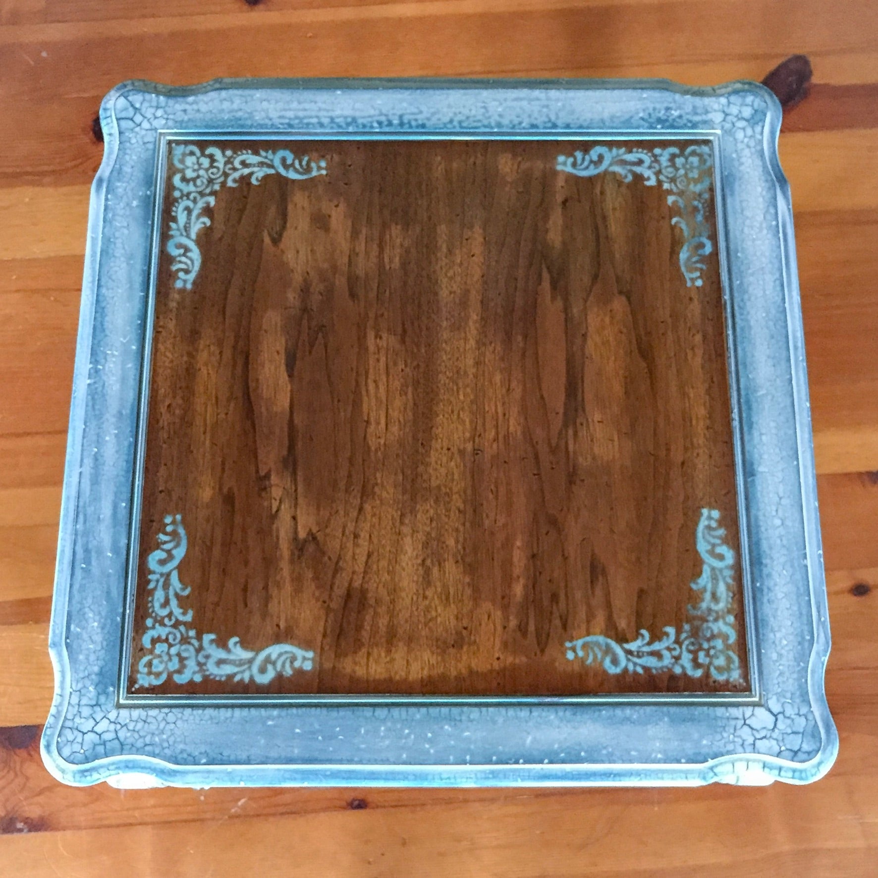 Birds eye view of the stained wood tabletop with damask accents at corners & distressed white trim.