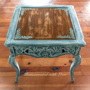 A French country style side table with curved legs, a stained wood tabletop & distressed white trim.