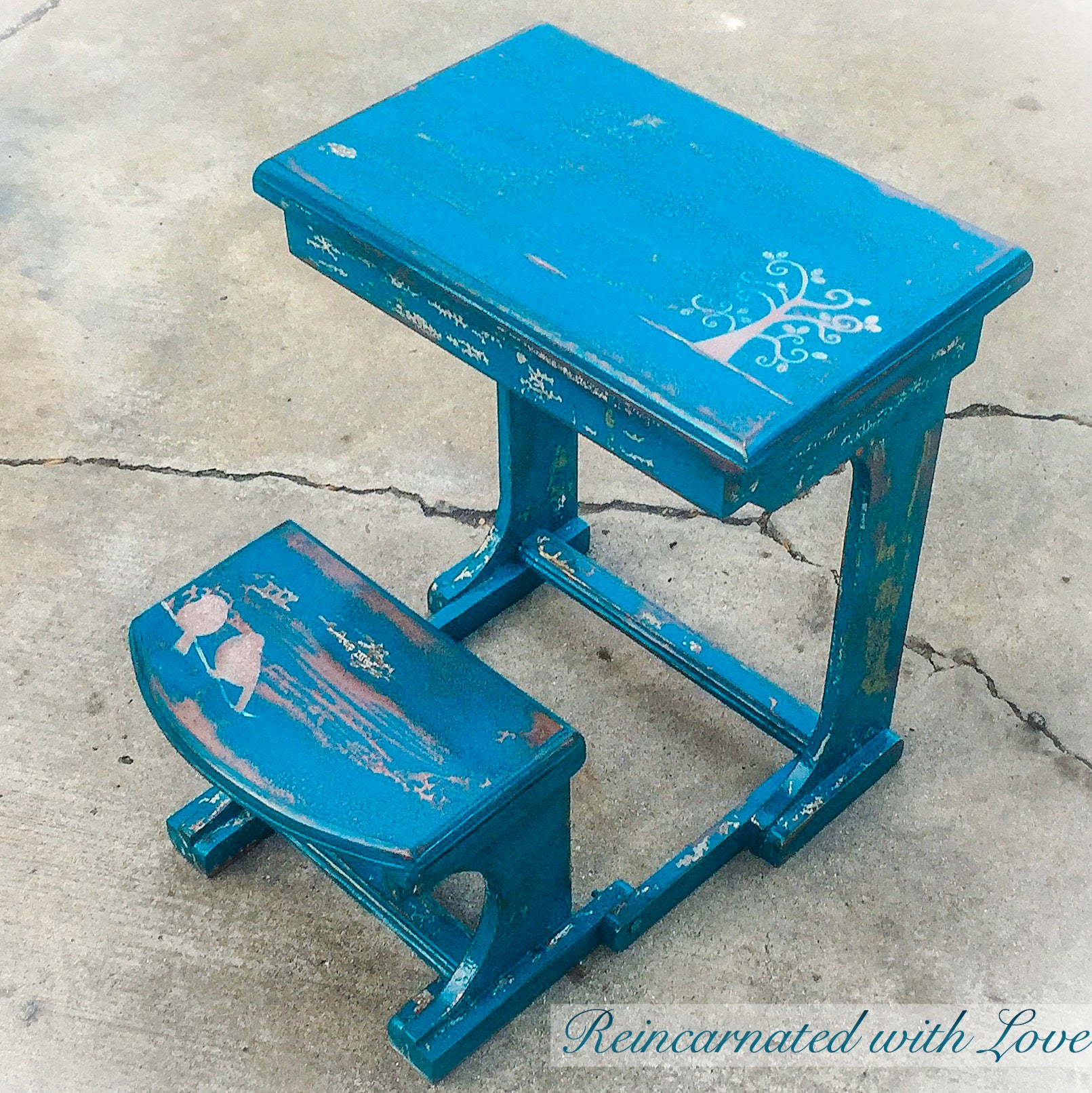 An antique, child’s desk made of solid wood. The desk is painted in a distressed, blue finish with small, bird accents.