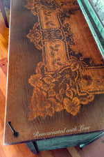 Close up of the tabletop on a farmhouse style, dressing table, with green, patina trim, stained wood & lace accents.