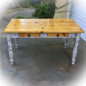 A farmhouse table, made of solid pine, with a stained, wood tabletop & a distressed white base.