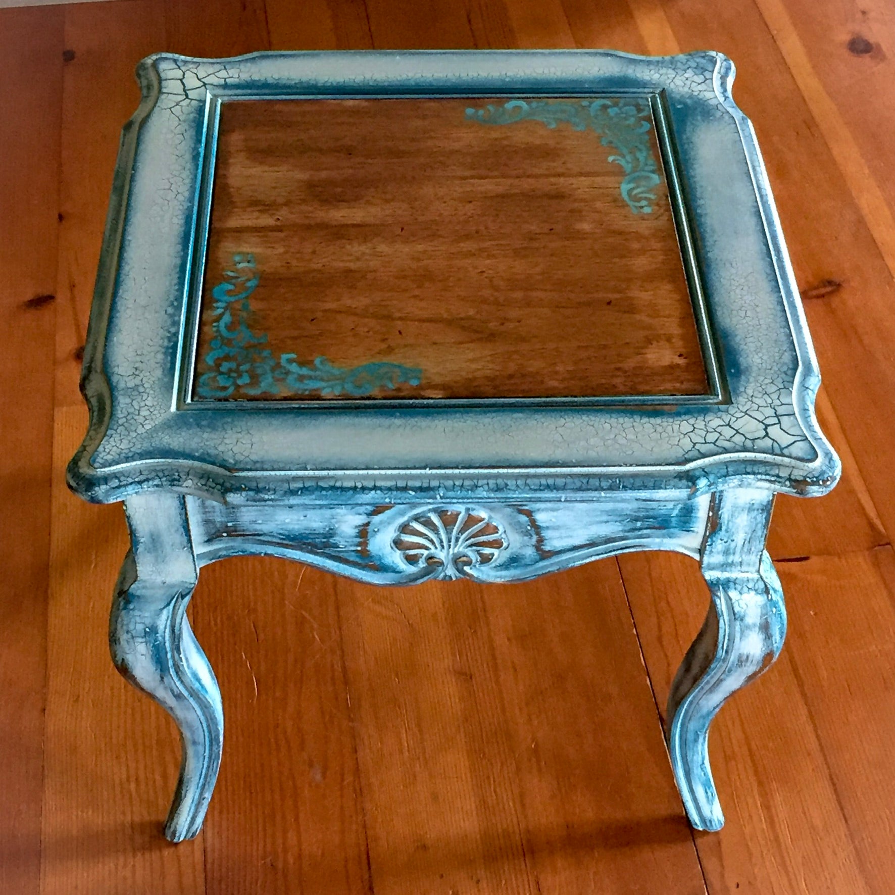 A French country style, end table with damask accents, a stained wood tabletop & distressed, white trim with blue undertones.
