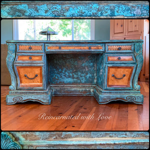 Front view of an art nouveau style desk, with a blue & green, patina finish, on stained, solid wood.