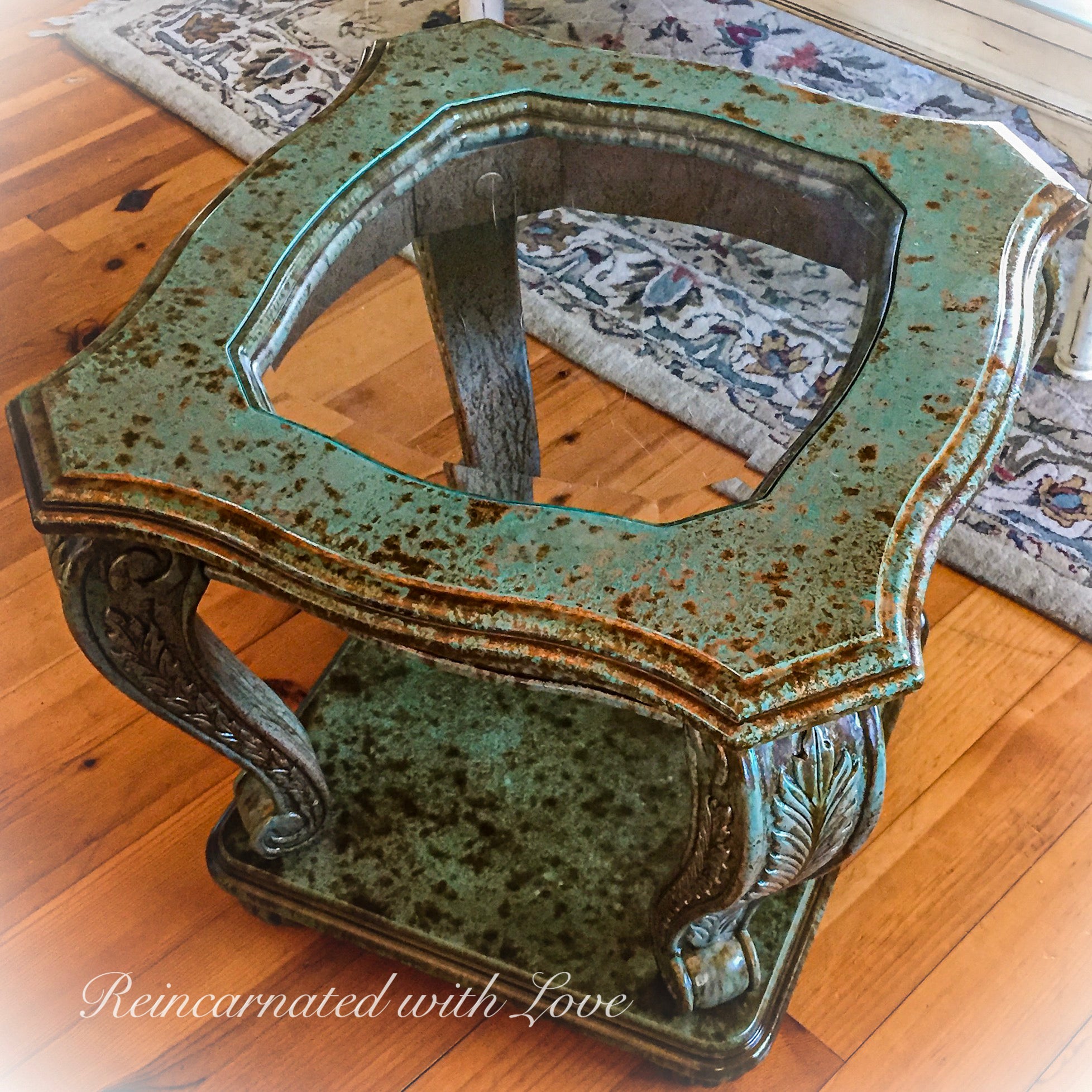 Solid wood, glass top, end table, done in a rusted copper, green patina finish, with vine accents carved into the table legs.