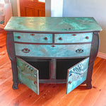 A boho style dresser, refinished in copper patina & rusted iron, with three drawers & a large cabinet area on the bottom.