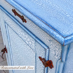 A close up of the hampers’s iron rusted hardware & distressed finish, in white with blue hues.