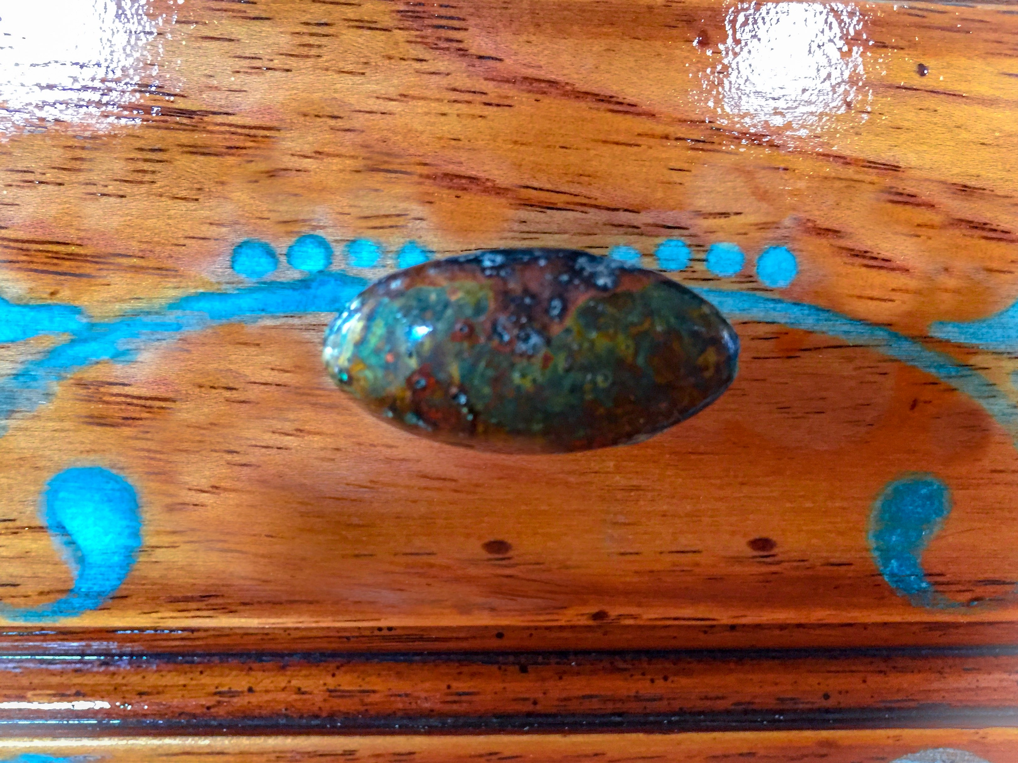 A close up of the drawer on an end table, in stained wood with white & blue accents & a patina, drawer pull.