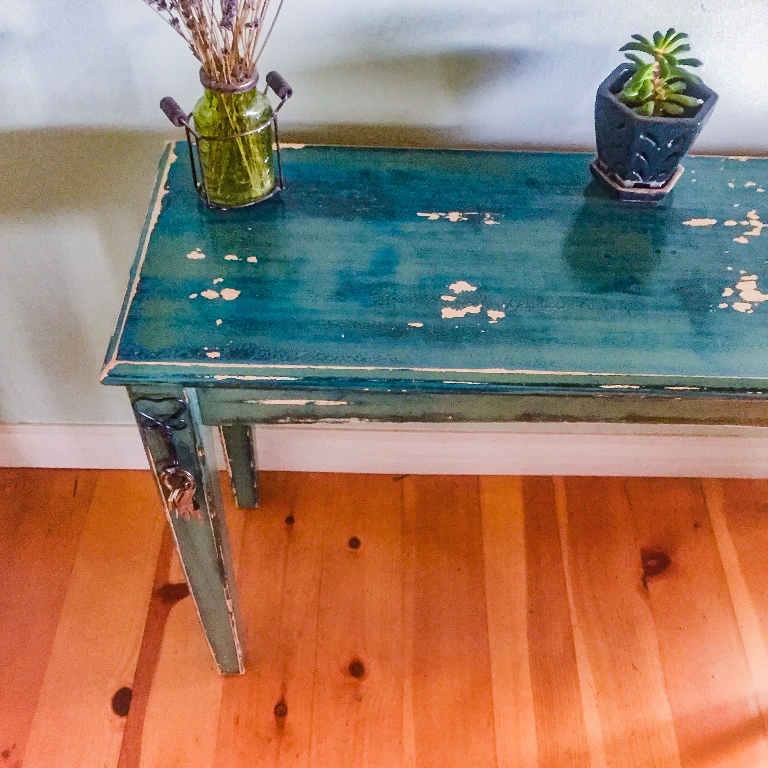 A small, entryway table with heart shaped, key hooks. The table is painted in distressed blue & green hues over solid wood.