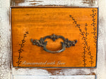 close up of a stained wood drawer face on an antique vanity, done with burnt wood floral accents & antique drawer pulls.