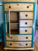 A boho style armoire with mirrored cabinet & six drawers painted in distressed green on stained wood