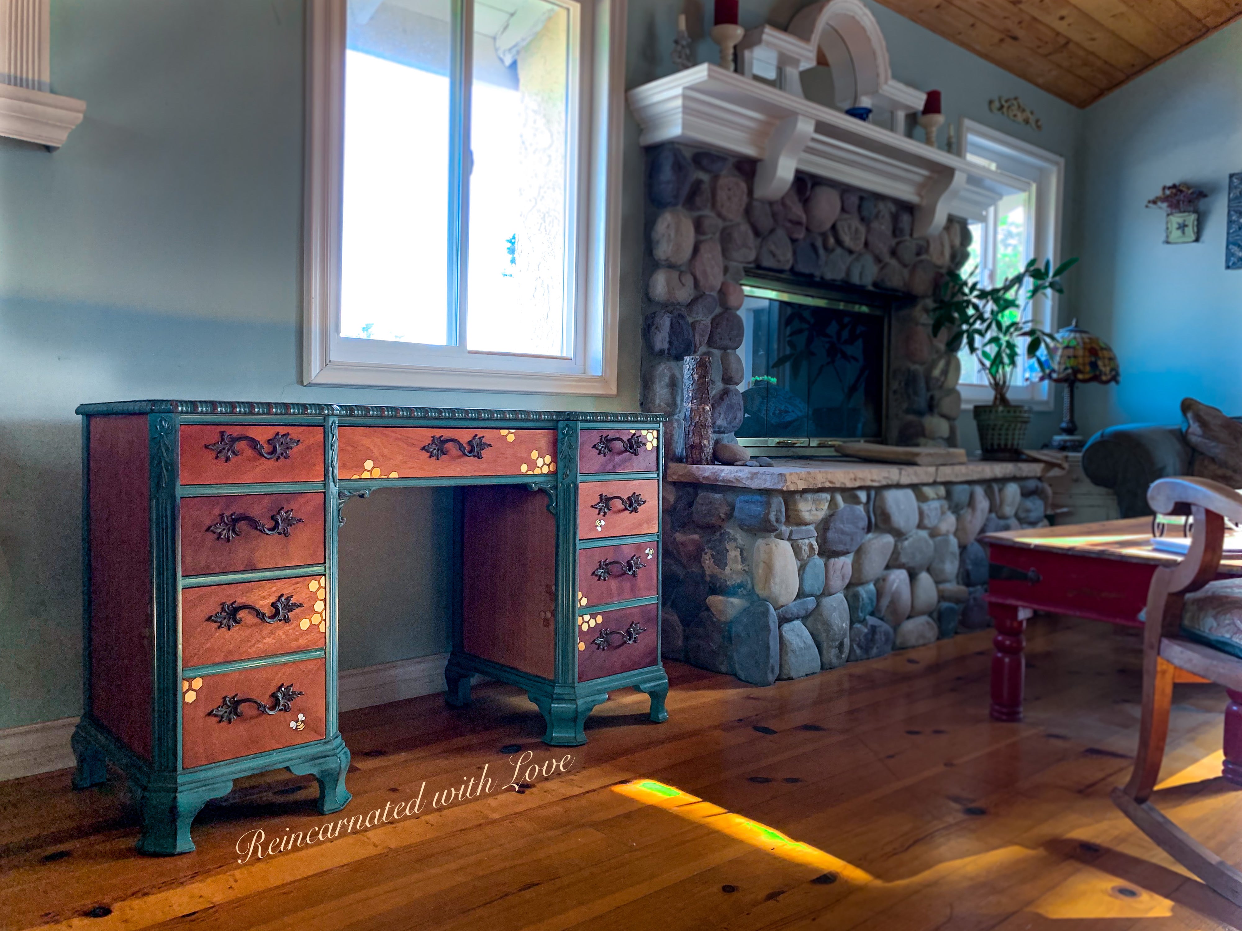 A stained wood desk with distressed green trim, accented with iridescent  honeycomb & tiny bees.