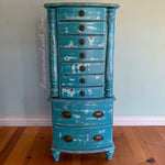 A free standing jewelry armoire painted in distressed blue with velvet lined drawers.