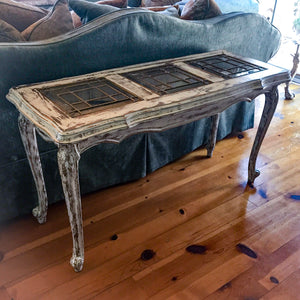 A French country style sofa table in distressed white with glass panels.